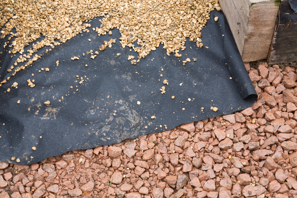 Landscape fabric laid on top of rocks and underneath gravel.