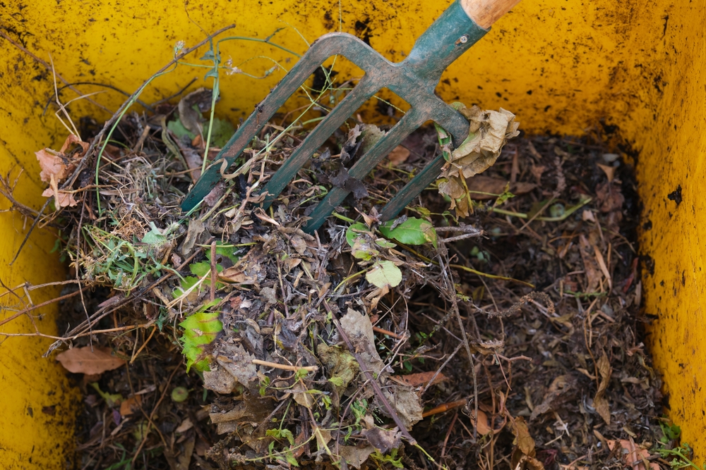 A closeup of someone turning compost in a yellow bin.