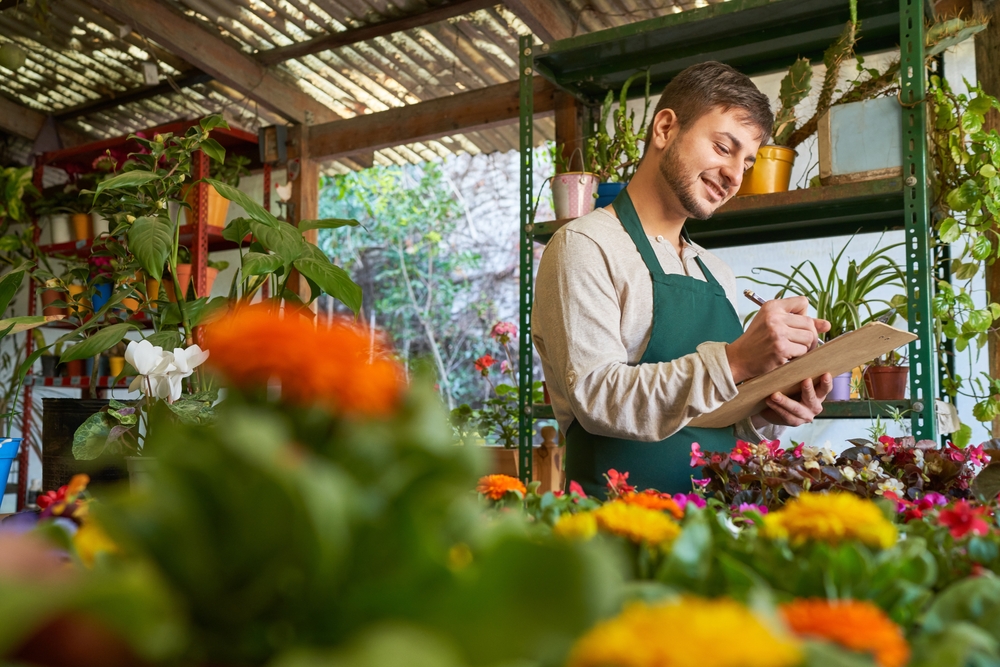 A young male florist using a checklist for his flower shop.