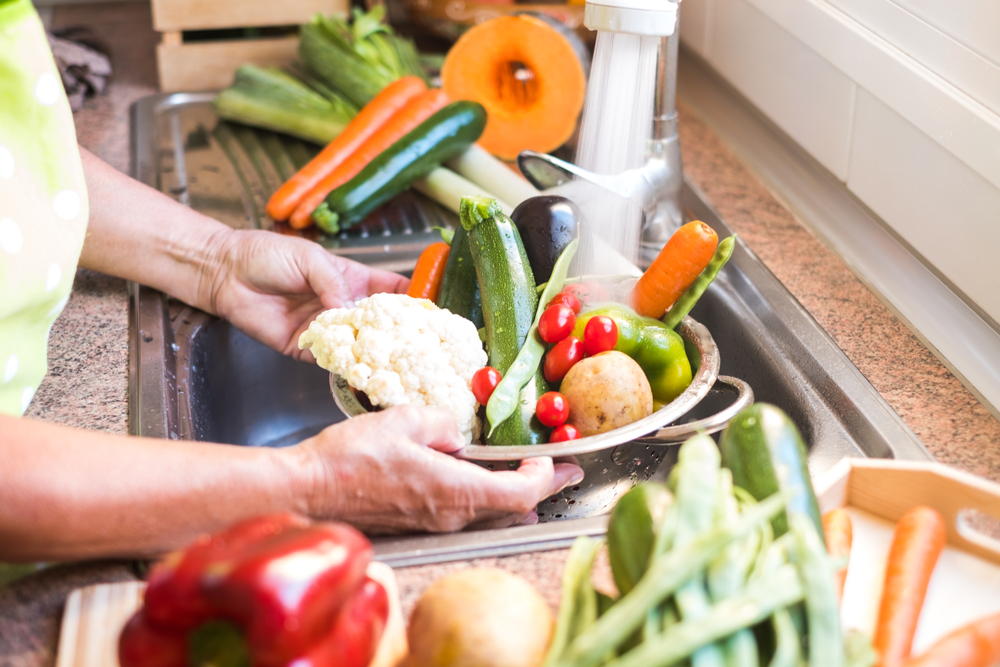Someone washing vegetables in a bowl in their sink.