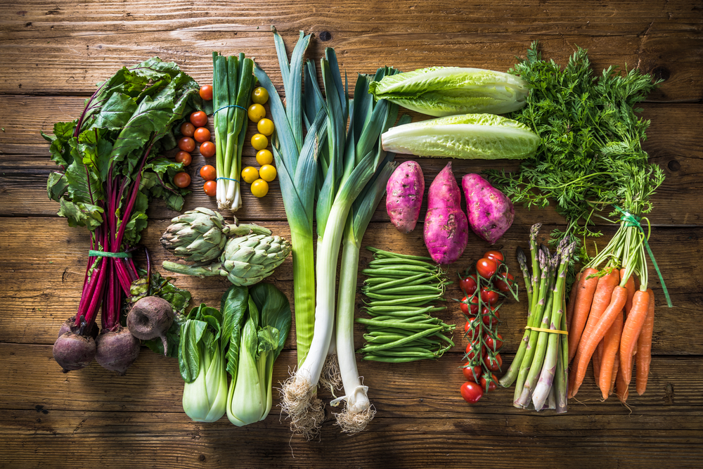 Various vegetables, such as lettuce, carrots, asparagus, and more, arranged on a wooden table.