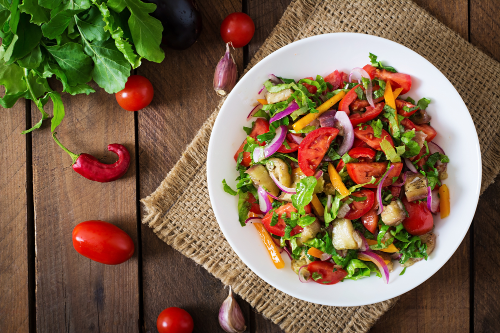 A plate bowl of various vegetables on a wooden table.